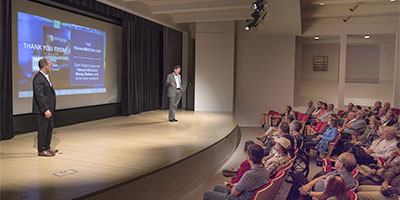 Pat McClain giving a live presentation on a stage in front of an audience