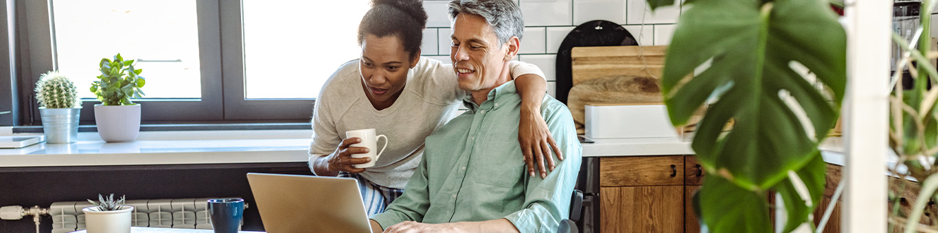 middle-age couple smiling and looking at a laptop while sipping coffee